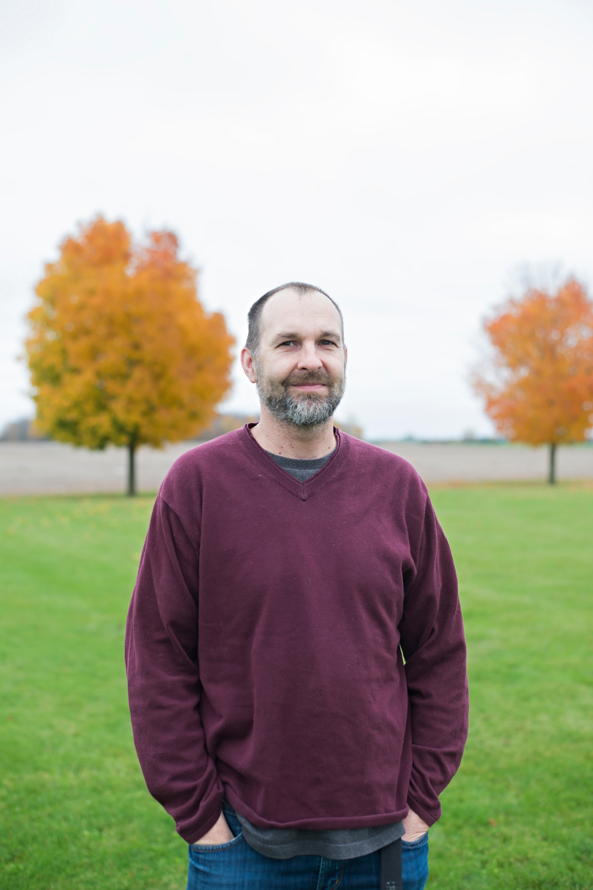 Man in red sweater with a colourful tree in background