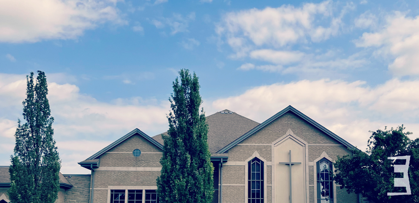 church building with fluffy white clouds green trees E logo