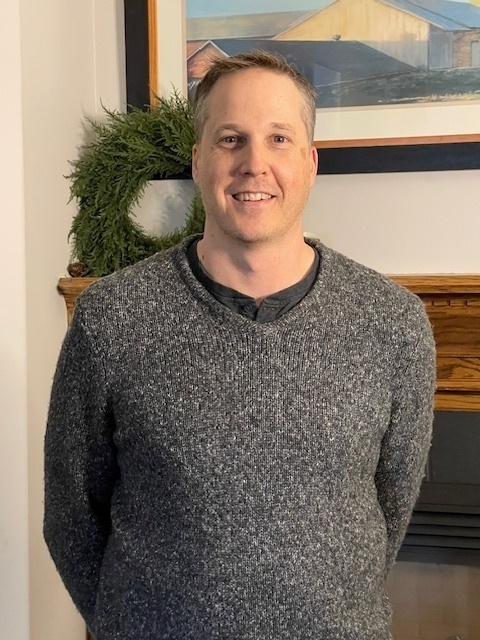 headshot of man in front of fireplace