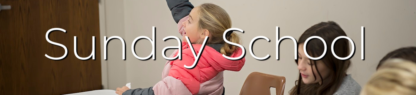 Girl raising hand at a table, young girl looking down, white lettering